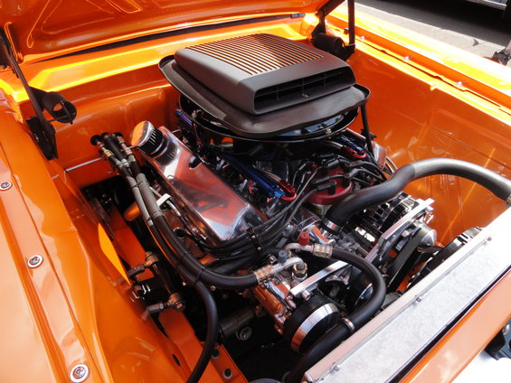 Close-up of a V8 engine with a chrome air cleaner and a black hood scoop, set against an orange engine bay