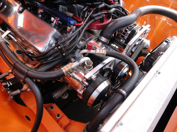 Orange vehicle engine bay with chrome valve covers, red distributor cap, and black hoses