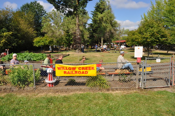 Yellow miniature train with people riding on a track, behind a fence