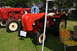 1959 Kenworth W900A - Two vintage red tractors are displayed outdoors on a sunny day, with one in the foreground and another partially visible behind it.