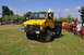 1959 Kenworth W900A - A yellow Mercedes-Benz Unimog truck is displayed at an outdoor event with other vehicles and people in the background.