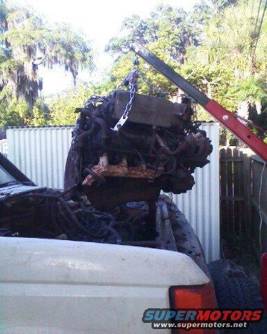Engine being lifted from a white pickup truck bed by a red crane