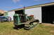 1959 Kenworth W900A - A green crawler tractor with "SIXTY" visible on its grille is parked outside a metal building, with another blue tractor in the background.