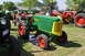 1959 Kenworth W900A - A green and yellow tractor with red wheels is parked on grass at an outdoor event with other tractors visible.