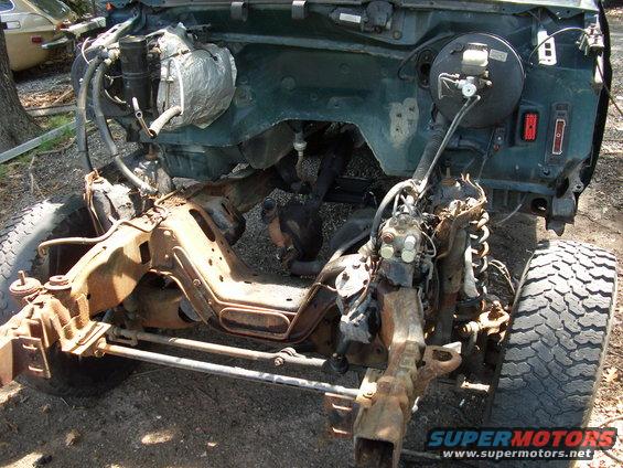 Partially disassembled vehicle chassis with engine components visible. Frame is rusty