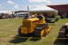 1959 Kenworth W900A - A yellow Caterpillar tractor is displayed on a grassy field with tents and people in the background.