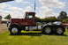 1959 Kenworth W900A - A maroon semi-truck is parked on a grassy field under a partly cloudy sky.