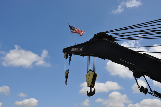 Crane boom with American flag and Bucyrus-Erie marking against a blue sky with clouds