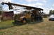 1959 Kenworth W900A - A weathered yellow truck with a large boom attachment sits in a field, with a modern SUV nearby.