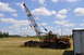 1959 Kenworth W900A - An old orange crane truck sits idle in a field, its boom extended against a bright blue sky with fluffy clouds.