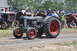 1959 Kenworth W900A - A Case tractor is driven on a dirt path during an outdoor event, with spectators and other vintage machinery present.