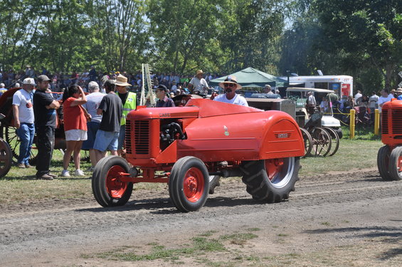 Red tractor with a driver, seen from the front-right at an outdoor event