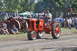 1959 Kenworth W900A - An orange tractor carries two passengers during an event, with spectators in the background.