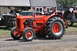 1959 Kenworth W900A - Two people ride in an orange Case tractor at an outdoor event with other farm equipment.