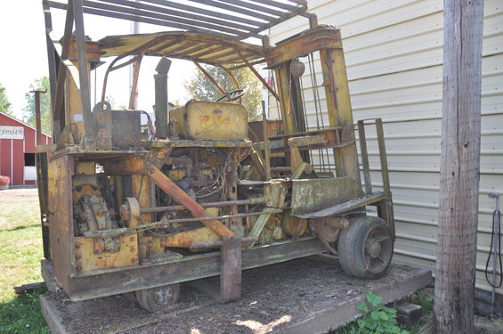 Rusty yellow forklift with exposed engine and worn tires, viewed from a three-quarter front angle