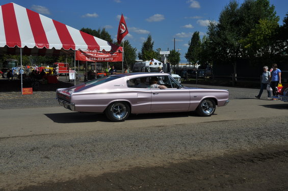 Pink 1966 Dodge Charger coupe driving past a red and white tent
