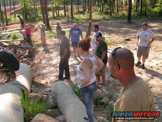 People gathered around large concrete pipes in a wooded area
