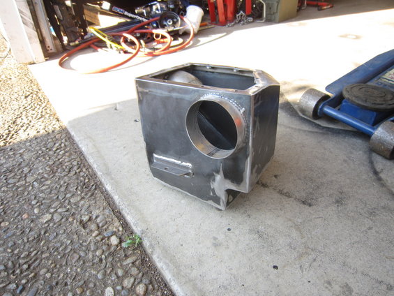 Custom metal intake box with circular opening, welded seams, and mounting tabs, resting on concrete