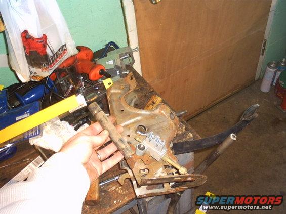 Hand holding rusty brake pedal assembly with various tools in background