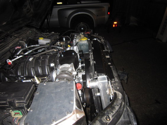 engine bay with supercharger and radiator, another vehicle in background