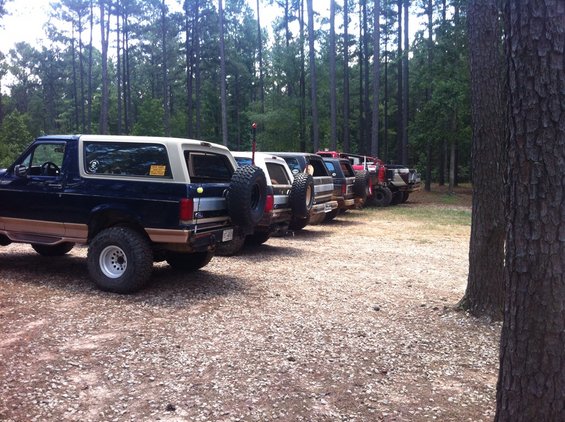 Dark blue and tan Ford Bronco with a spare tire mounted on the rear, parked in a line with other off-road vehicles