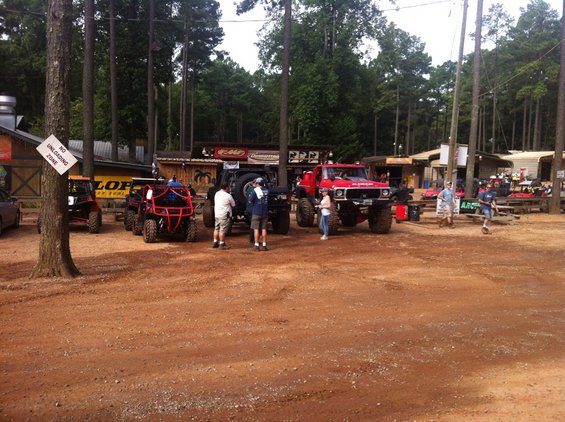 Red lifted truck with large tires parked on dirt, front view
