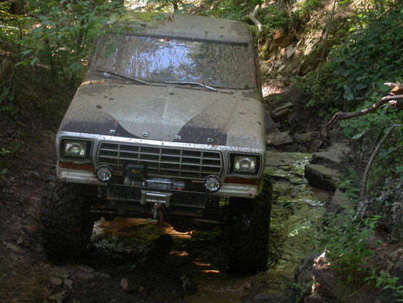 Mud-covered 1979 Ford F-150 driving through a creek with large tires and a winch