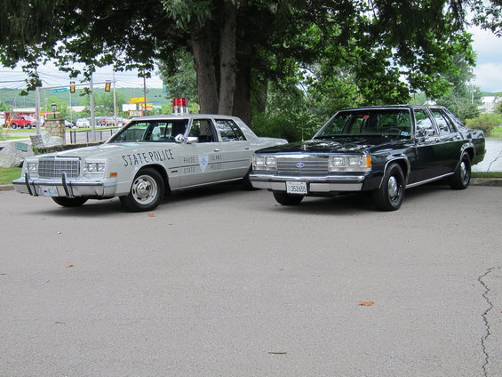 Dark blue Ford Crown Victoria and a light gray police car parked side-by-side