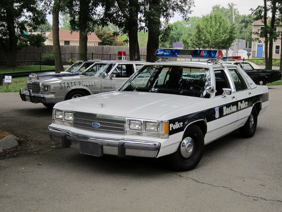 White 1991 Ford Crown Victoria police car with black stripe and 'Boston Police' text, parked in front of another police car