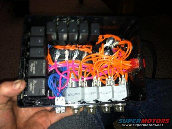 Close-up of a vehicle's aftermarket fuse box with multiple relays and orange wiring