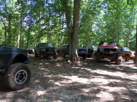 Several lifted trucks parked in a dirt clearing surrounded by trees