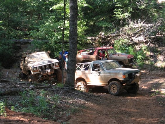 1979 Ford F-150 and two other off-road trucks on a dirt trail in the woods