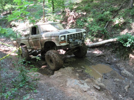 1979 Ford F-150 with large tires navigating a muddy trail in the woods