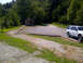 1982 Ford Bronco - A white SUV is parked on a gravel lot surrounded by trees and a small wooden building.