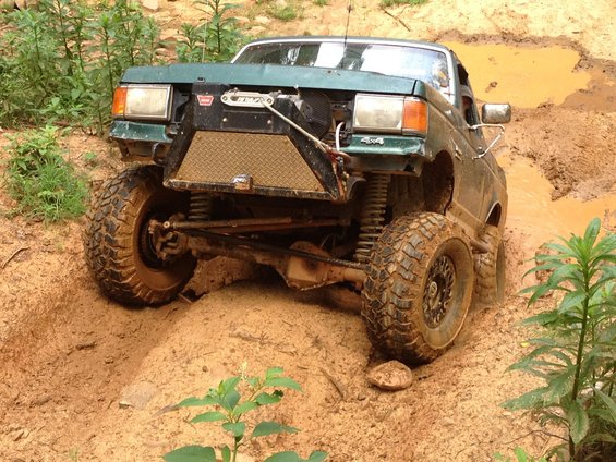 Green off-road truck with winch and custom bumper navigating a muddy trail