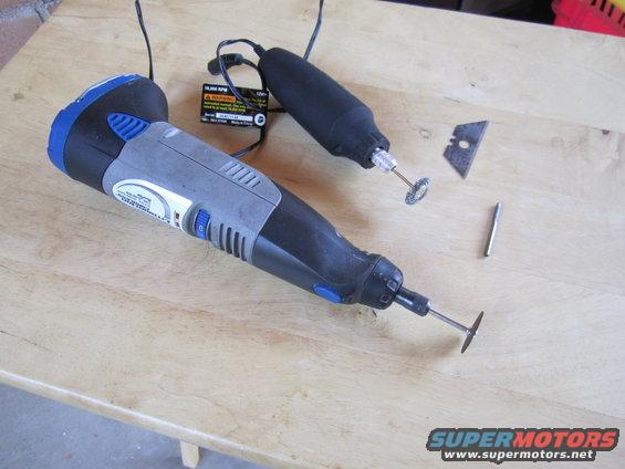 Two Dremel rotary tools with cutting discs, a razor blade, and a pin on a wooden surface