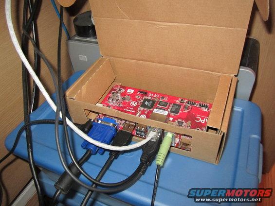 Red circuit board with various cables connected, inside a cardboard box