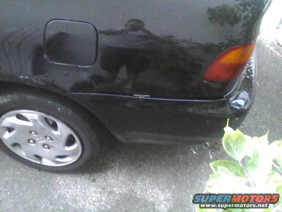 Rear quarter panel and bumper of a black sedan. Shows gas cap door and taillight