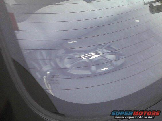 Car wheel with a silver emblem, seen through a rear window