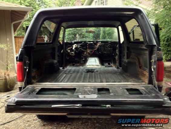 Rear view of a 1987 Ford Bronco with interior stripped out, showing exposed wiring and empty cargo bed