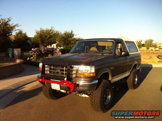 Dark brown Ford Bronco with a red bull bar and lifted suspension, parked on a street