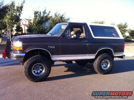 Dark brown 1992 Ford Bronco with a white top, lifted suspension, and off-road tires, seen from the side