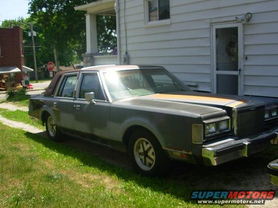 Gray 1988 Lincoln Town Car parked on grass next to a white house
