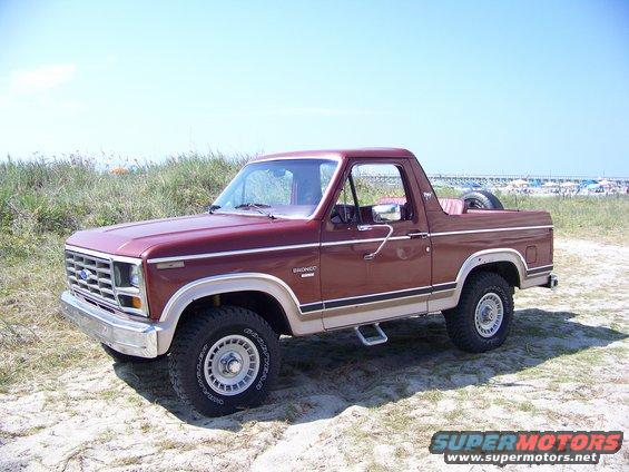 Maroon Ford Bronco parked on a sandy area with beach in background