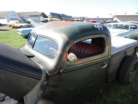 Old dark green pickup truck with red interior and a number 44 on the roof. Other cars are parked in the background