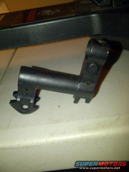 Close-up of a black metal gun part with a cylindrical body and a bracketed end