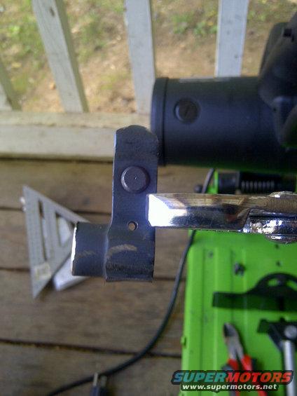 Metal bracket with bolt attached to a shiny rod, with a green machine and a speed square in the background