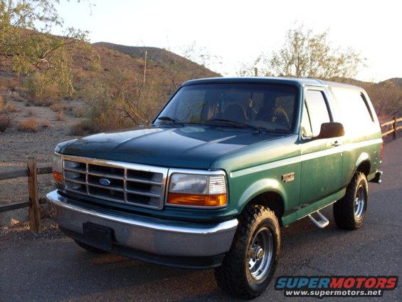 Green 1996 Ford Bronco, front 3/4 view, parked on dirt road with wooden fence