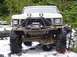 1989 Ford Bronco - A heavily modified Ford Bronco navigates a snowy, rocky trail in a wooded area.
