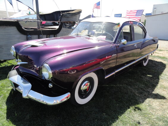 Purple Kaiser sedan with a white roof, parked on grass. American flags are on the roof